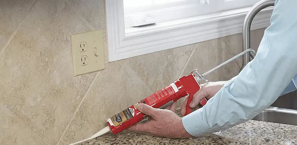 Handyman applying caulk along a kitchen backsplash and countertop seam in Chula Vista, CA
