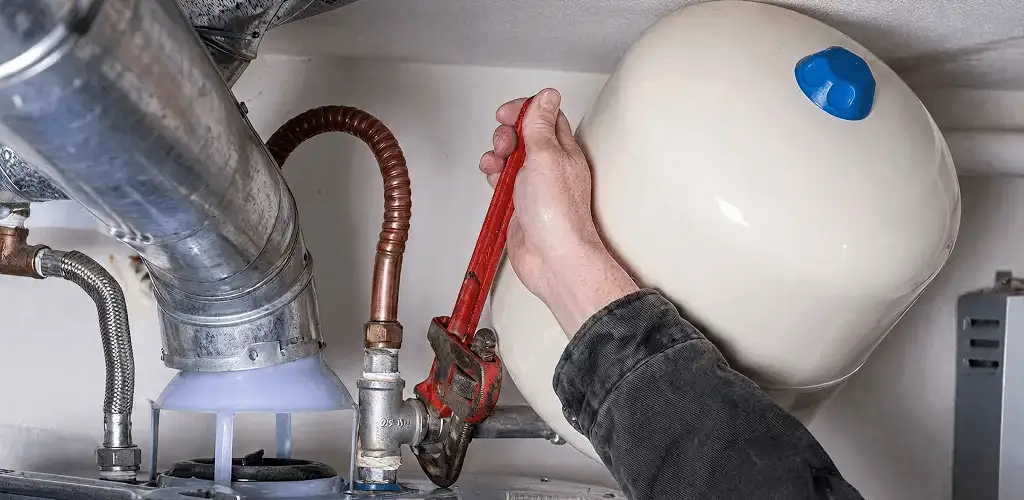 Water heater repair technician tightening plumbing connections near a tank unit in Chula Vista, CA